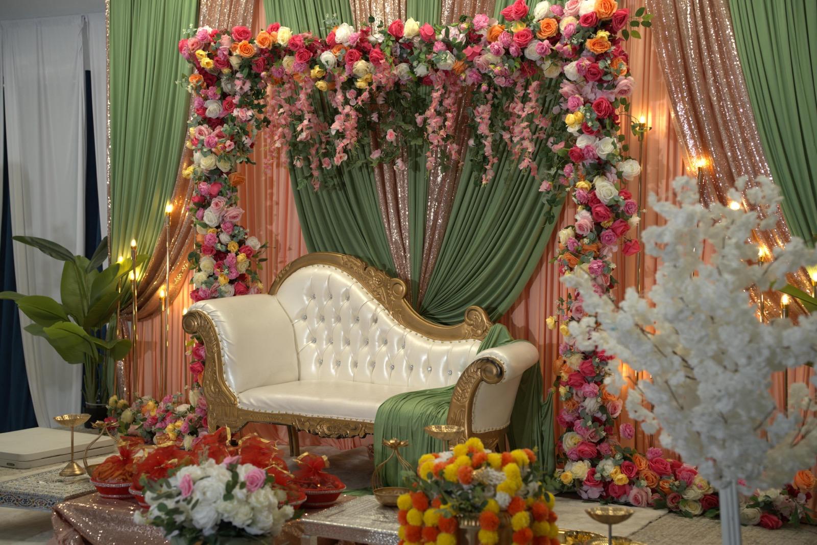Wedding stage with a floral arch and gold loveseat backdrop